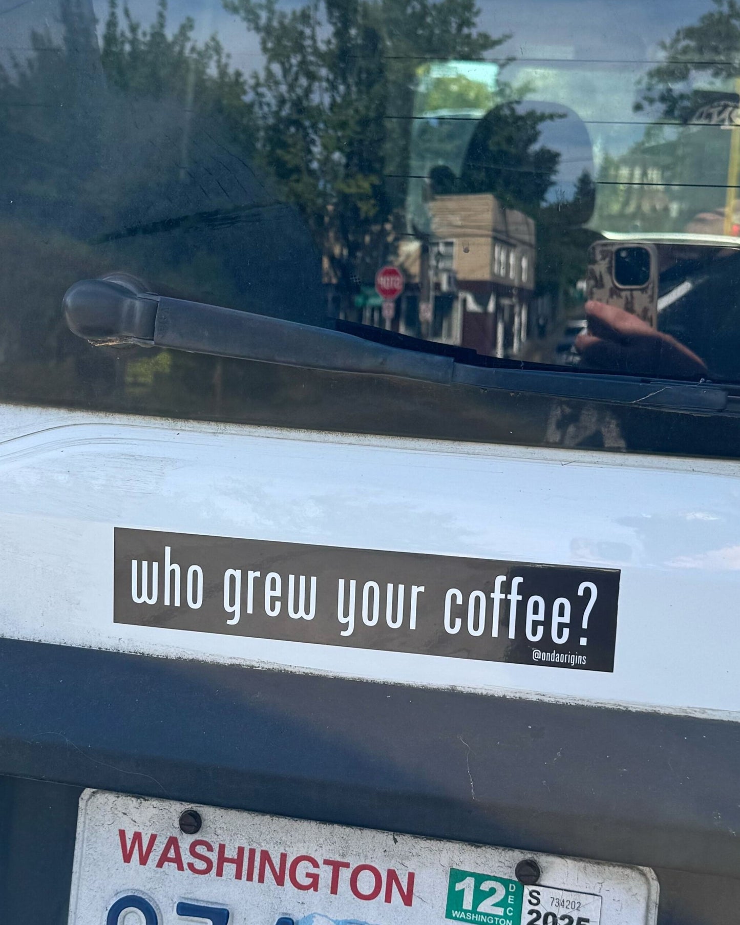 Car window with a sticker reading 'who grew your coffee?' and a Washington state license plate.